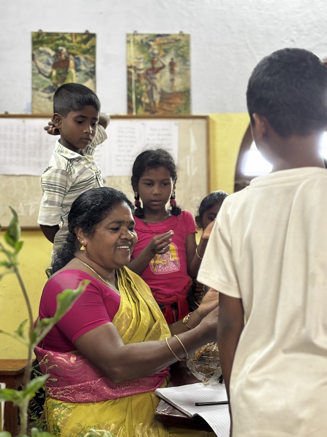 Smiling teacher in pink-and-yellow sari working closely with children around her in a classroom